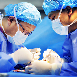 Two surgeons in blue gowns and gloved hands work on a patient.