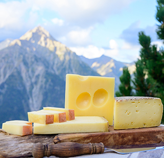 French beaufort, abondance, emmental, tomme de savoie cheeses served outdoor in Savoy region, with Alpine mountains in the background