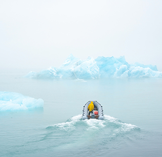 A scientist on a small boat on the ocean surrounded by icebergs.