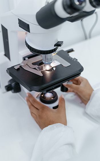 Closeup of a microscope in use with two hands are visible