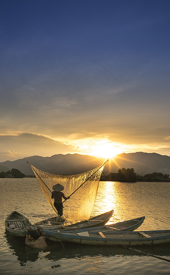 Fisherman on the Mekong River standing in a boat at sunset